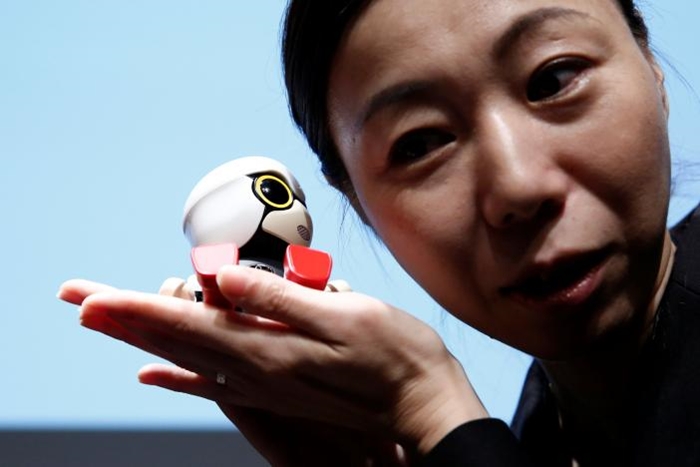 A staff member listens Toyota Motor Corp's Kirobo Mini robot's voice as she poses with the robot after a news conference in Tokyo